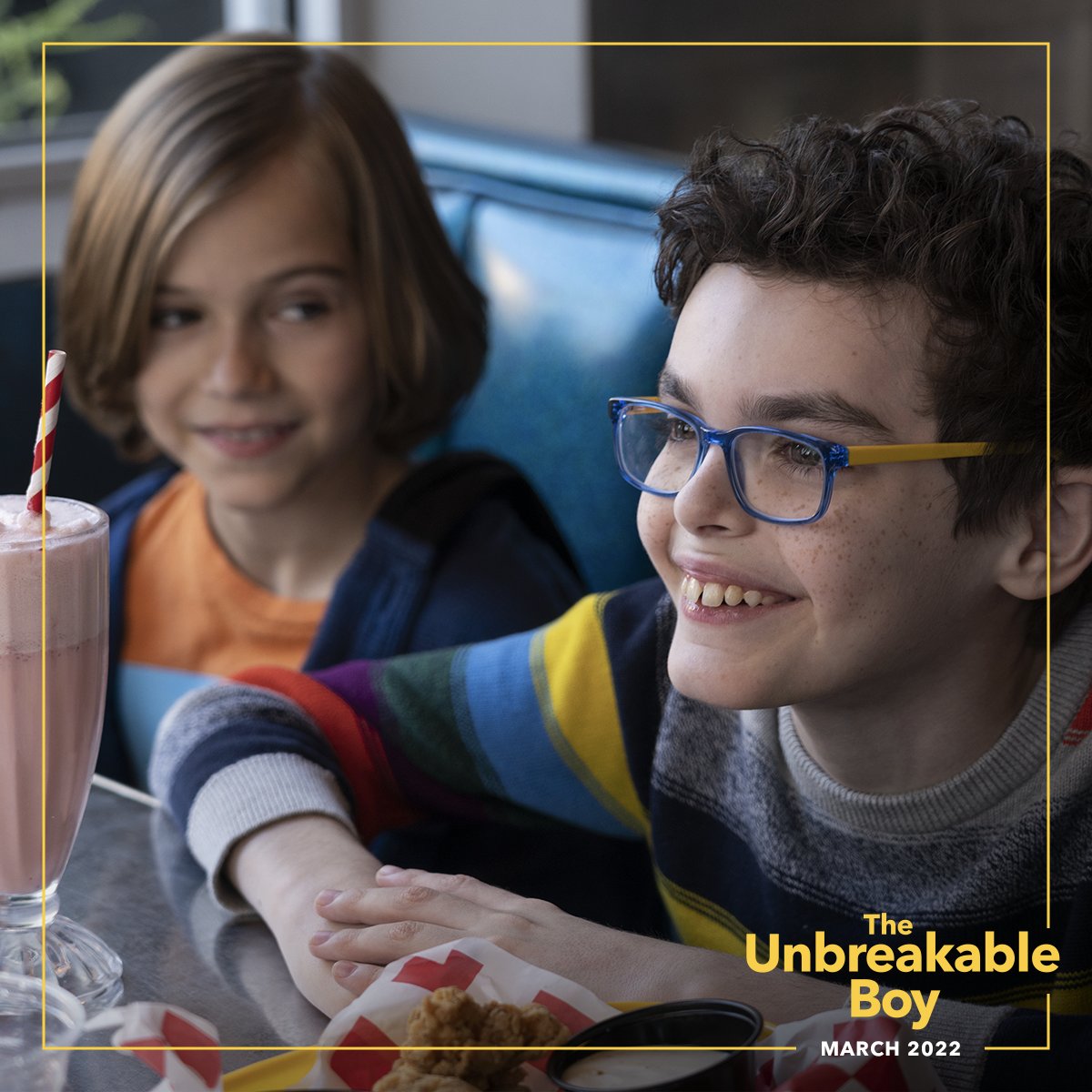 Austin, played by Jacob Laval, is seated next to his younger brother in a diner. Austin wears glasses and a striped sweater. There is a milkshake on the table in front of them, and both boys are smiling. In the corner right the movie title The Unbreakable Boy is visible. 