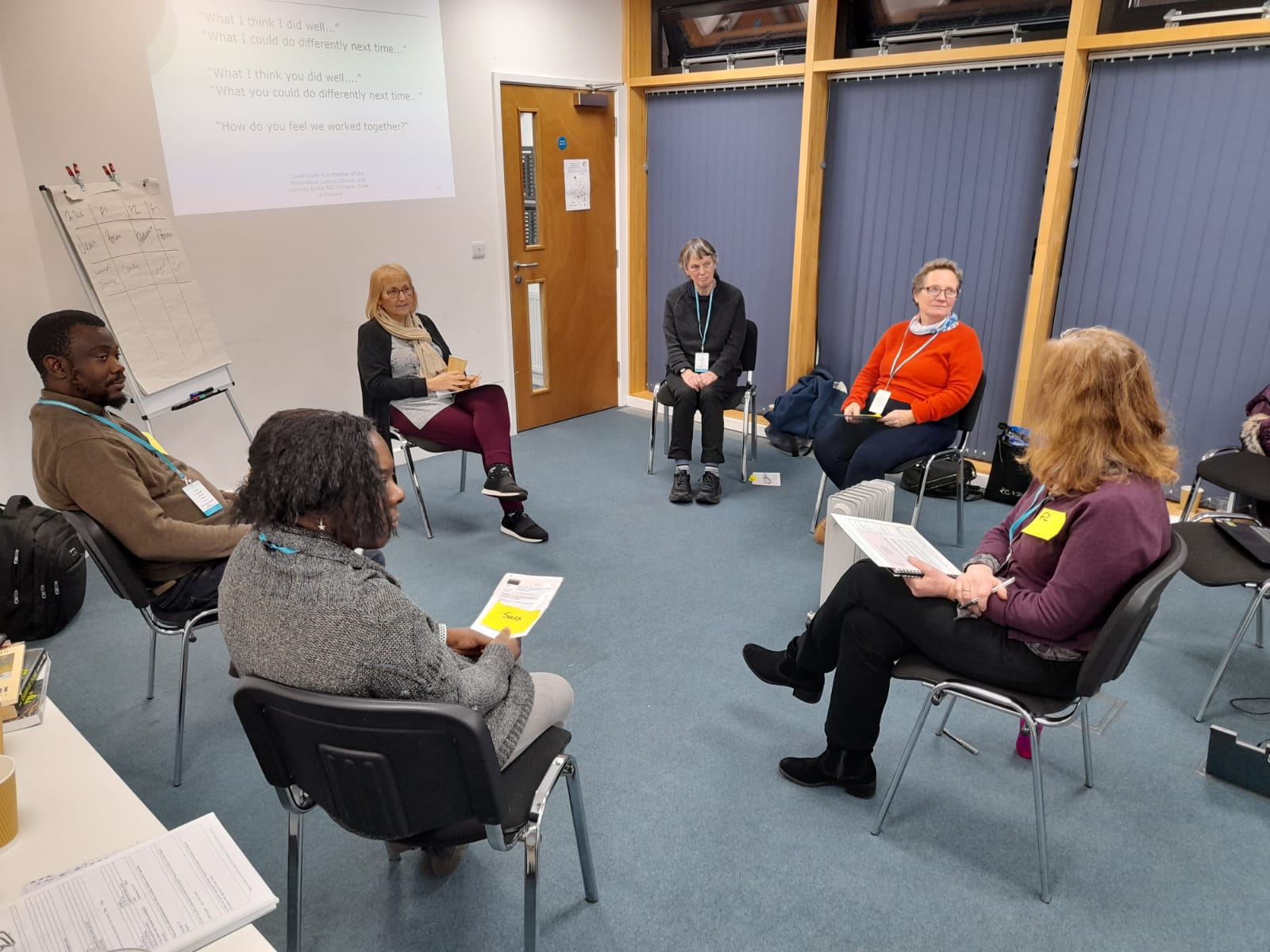 Six Restorative practitioners sit in a circle participating in a conference role play.