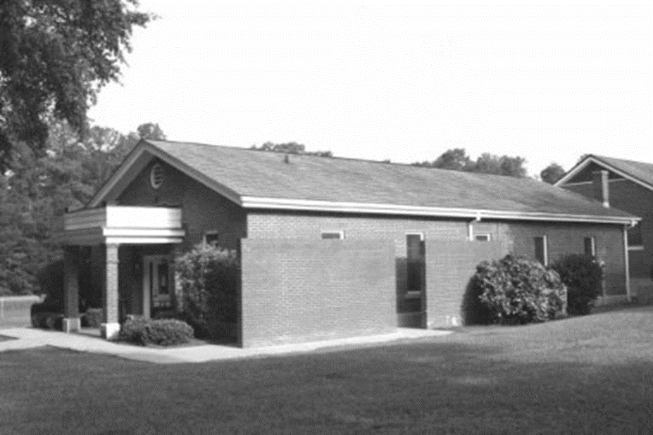 Brick building surrounded by shrubs and trees.