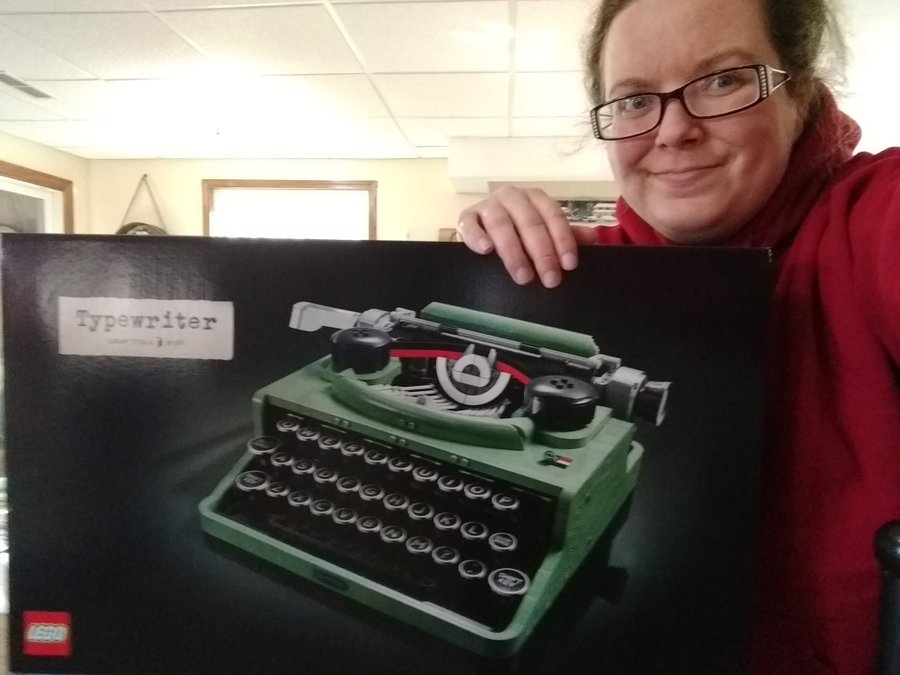 Me holding a box with a green Lego typewriter on it. It's taking up all the photo and then some with my head peeking in from the side.