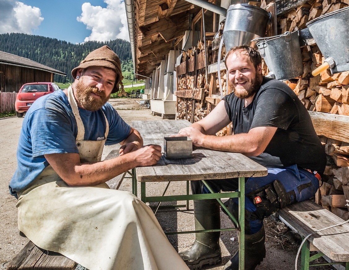 After the morning routine in the cow barn for milking and mucking out, the farmer and his farmhand enjoying a break in their sweaty stinking gear and boots.