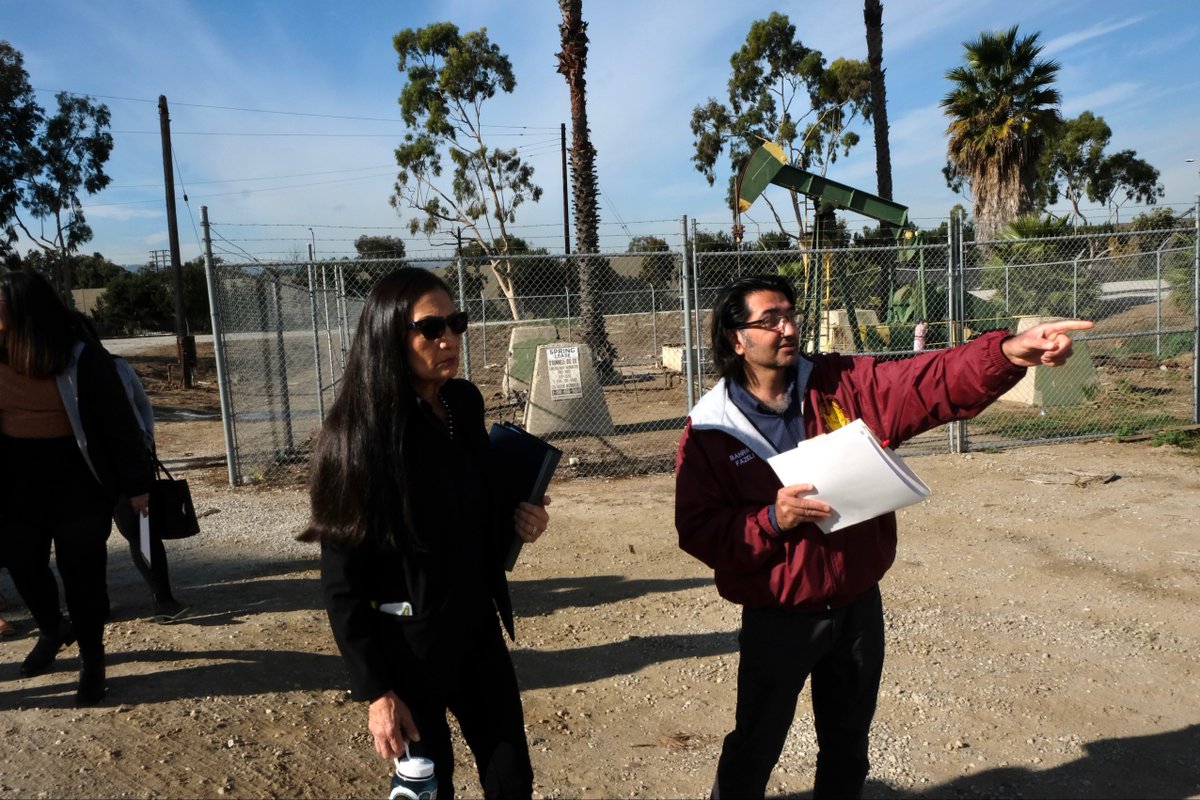 Secretary Haaland, left, stands next to a local leader, right, who is pointing. In the background, palm trees and an excavator.