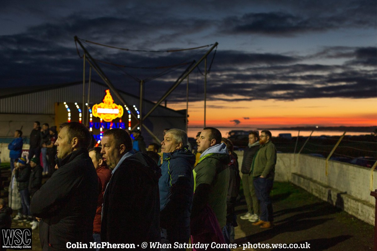 "Football supporters on a terracing on a winter’s afternoon, one of the great traditions of the game. At <a href="/ArbroathFC/">Arbroath FC</a> you can still simultaneously watch the game and get a glimpse into the world around you – in this instance the adjoining funfair and the North Sea"