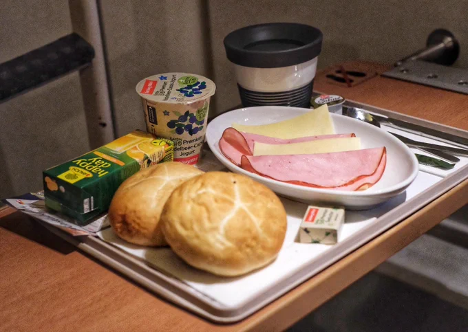 Picture of the breakfast with ham & cheese, bread rolls, orange juice, yogurt, a cup of coffee and a butter.
