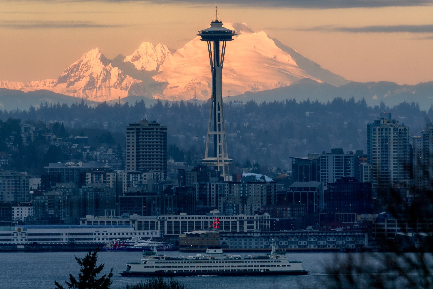 The Seattle space needle with Mount Baker in the background and a ferry sailing quietly by in the foreground