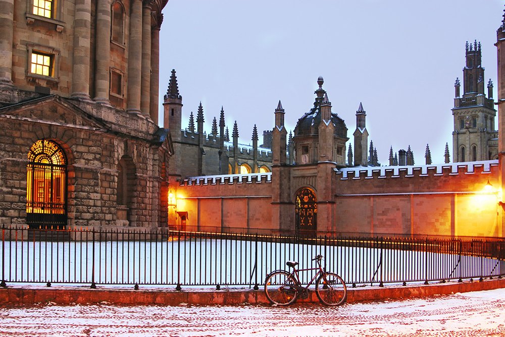 hazy skies behind the radcliffe camera, with snow on the ground behind a railing. A bike is propped up against it.