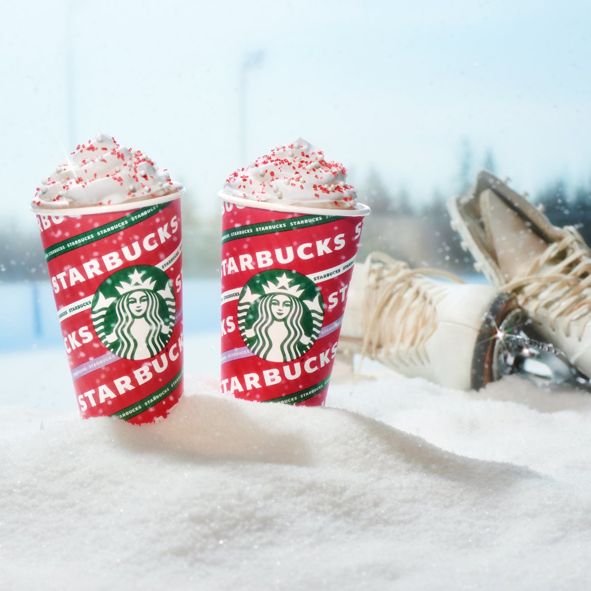 Two Toasted White Chocolate Mochas sit in the snow next to a pair of ice skates.