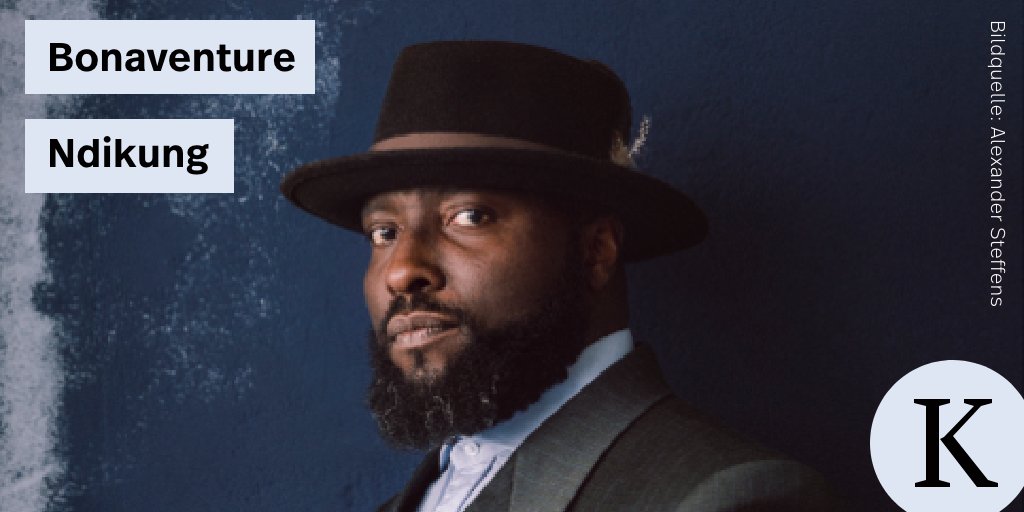 The picture shows a portrait of Bonaventure Soh Bejeng Ndikung. He is wearing a grey elegant suit, a bright blue shirt and a hat. 