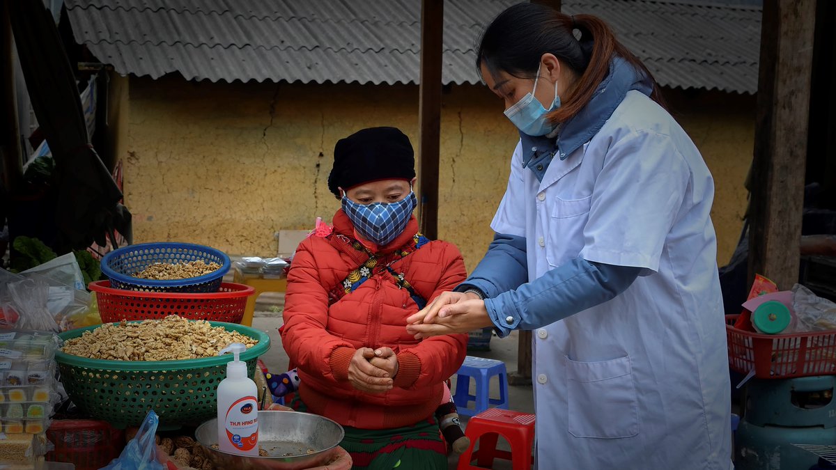at a market in Dong Van district of Ha Giang province: a health staff showing hand washing steps to a woman who are selling local products.