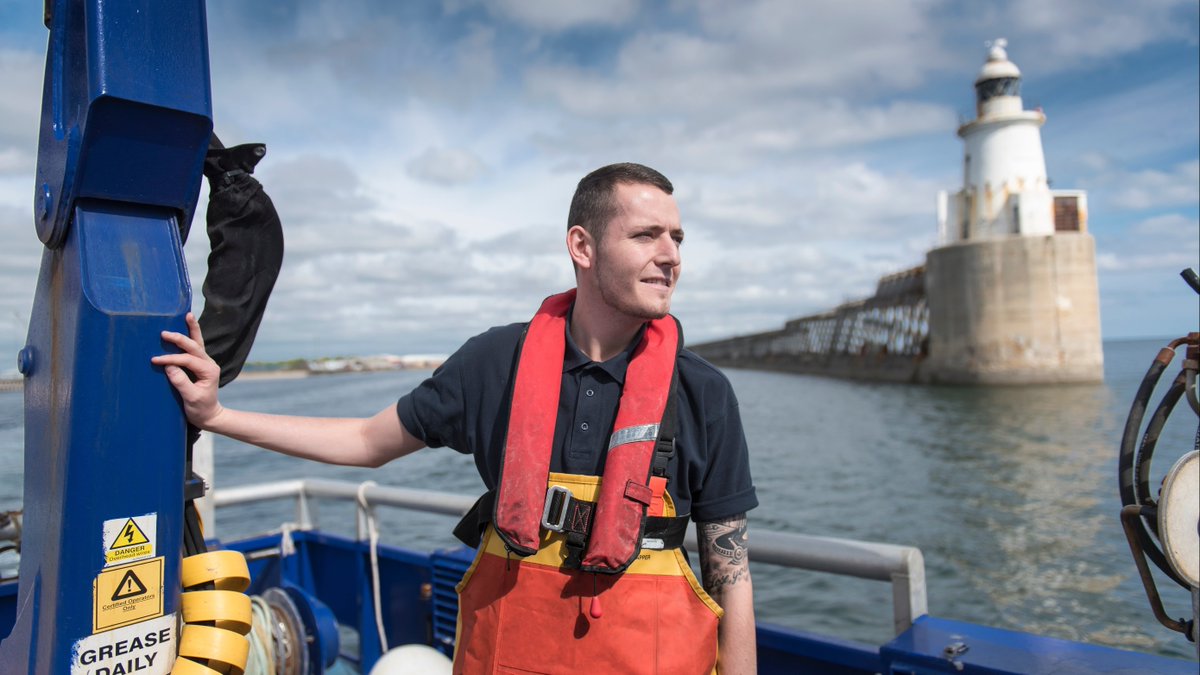 Caucasion fisherman on a boat looking to the right. A lighthouse is in the background