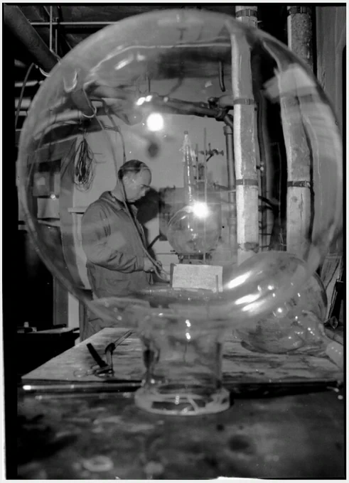 photo by Alicia Hills Moore (1951) "Worker in the MBL glassware department as seen through an inverted round flask. 2nd view with light reflection."