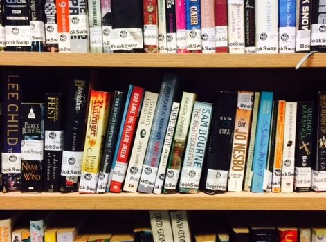 Three shelves of colourful books from the BookSwap, including Lee Child and Sam Bourne titles. 