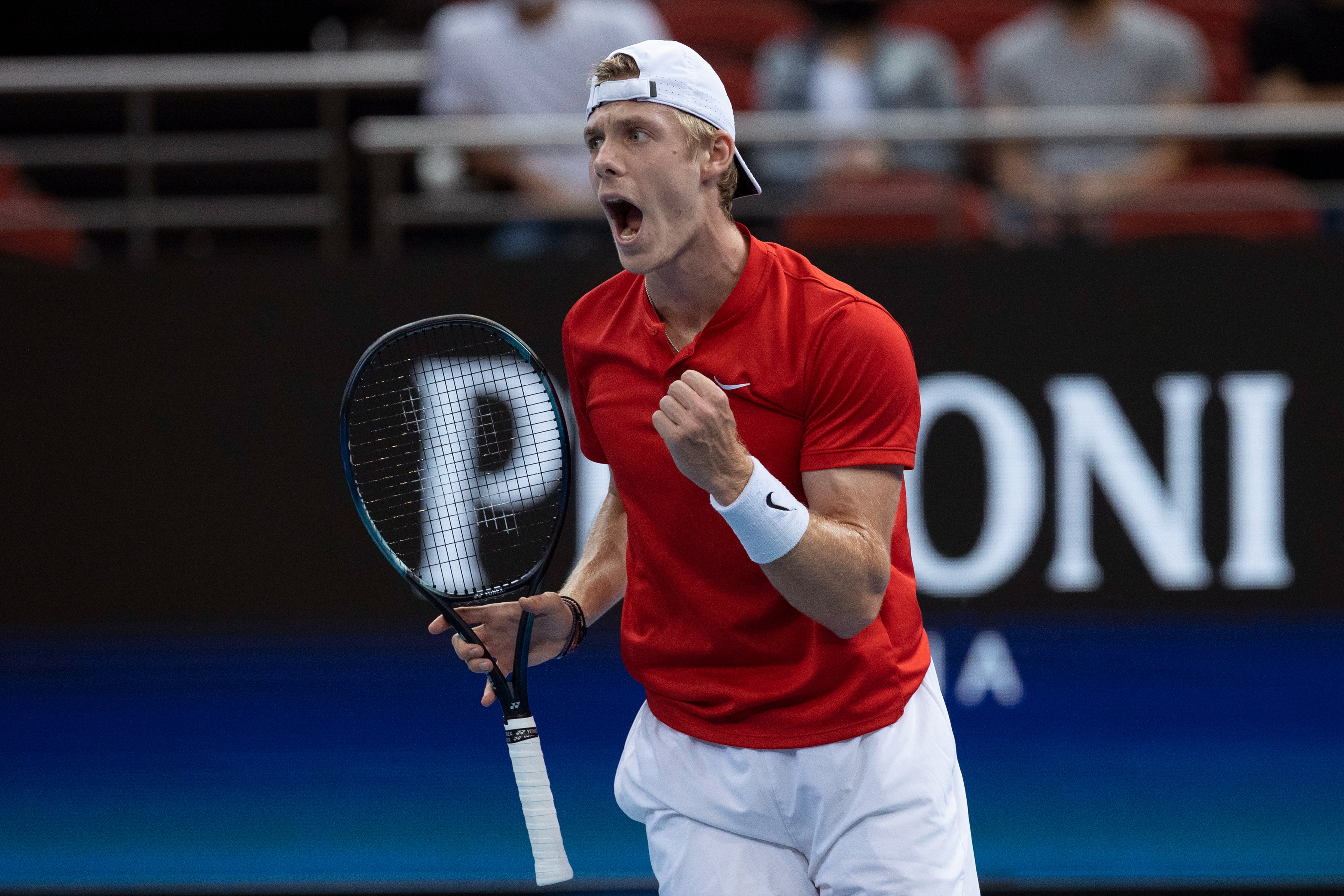 Tennis player holds racquet in one hand and makes a first pump with the other, while his mouth is open celebrating a win. 