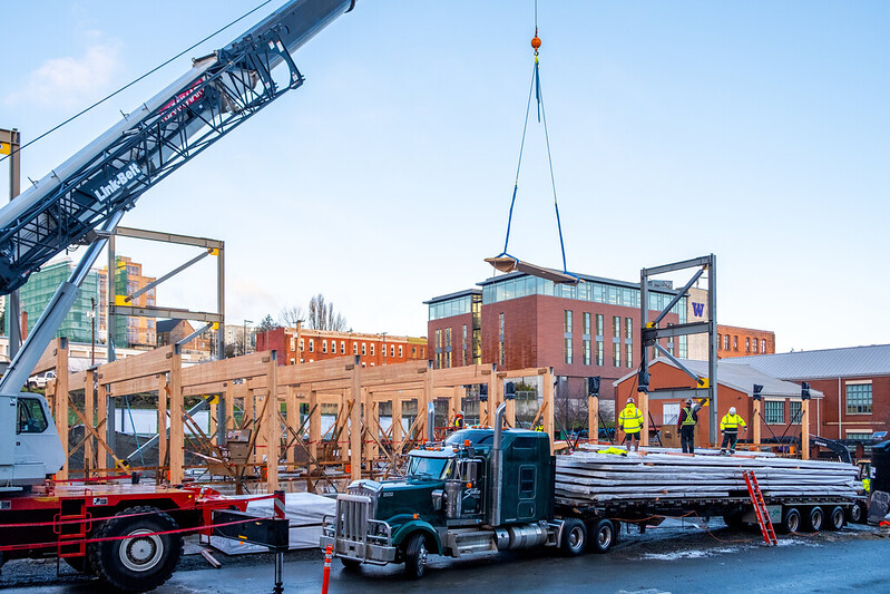 A crane lowers the first panel of cross-laminated timber to be installed at UW Tacoma's Milgard Hall construction site.