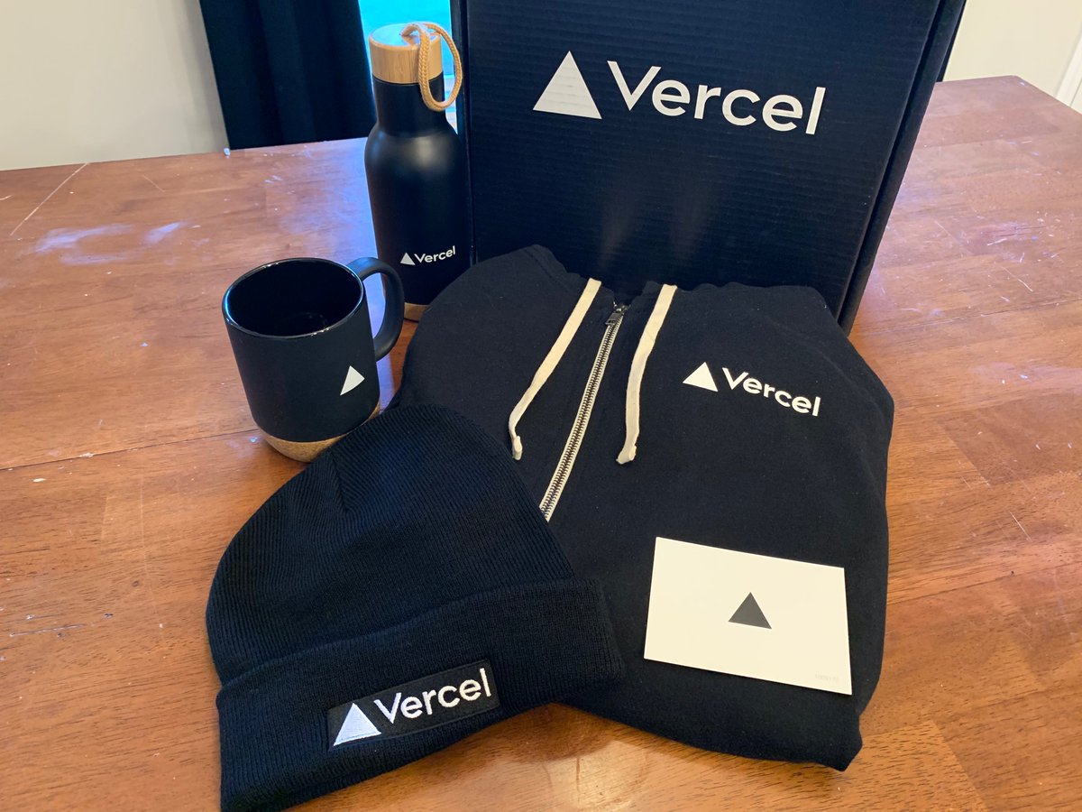 Mug, water bottle, hoodie, beanie, card in front of a box. All Vercel branded. 