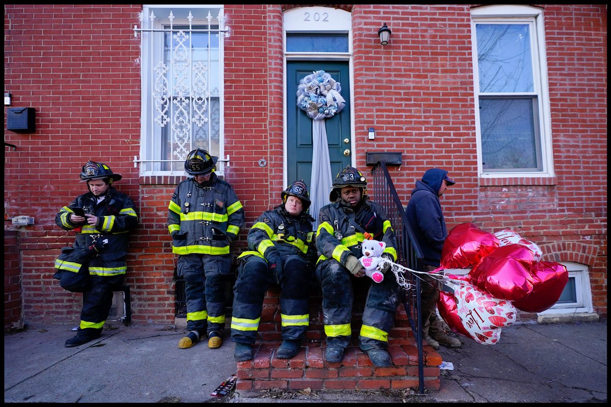 A Baltimore firefighter holds balloons given to him by neighbor Darlene Cucina as a group of fire officials sit on a stoop across the street where several firefighters died in a building collapse while battling a two-alarm blaze in a vacant row home , Monday, Jan. 24, 2022.