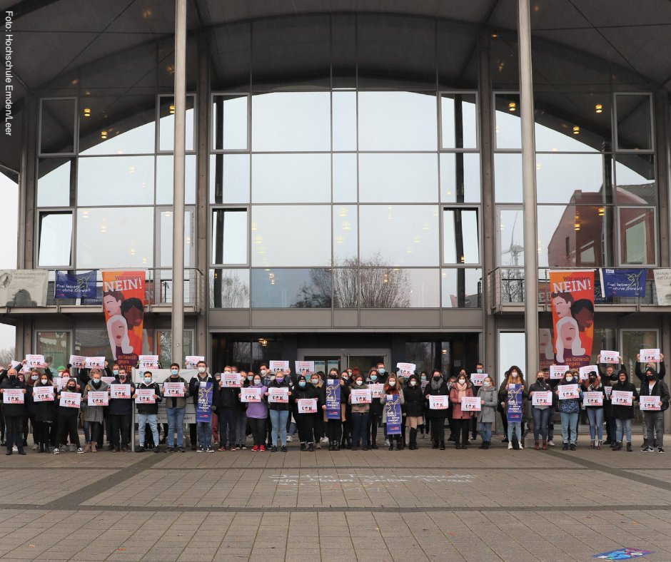 Studierende und Mitarbeitende stehen vor dem Eingang zur Hochschule Emden/Leer und halten Schilder zur Kampagne gegen Gewalt gegen Frauen in die Höhe. 