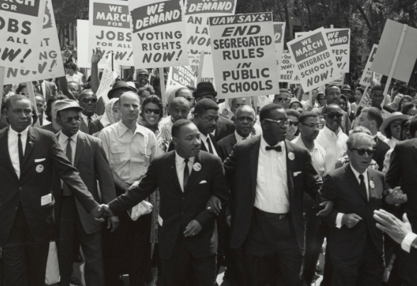 Leaders at the front of the March on Washington with arms linked and a crowd with signs following