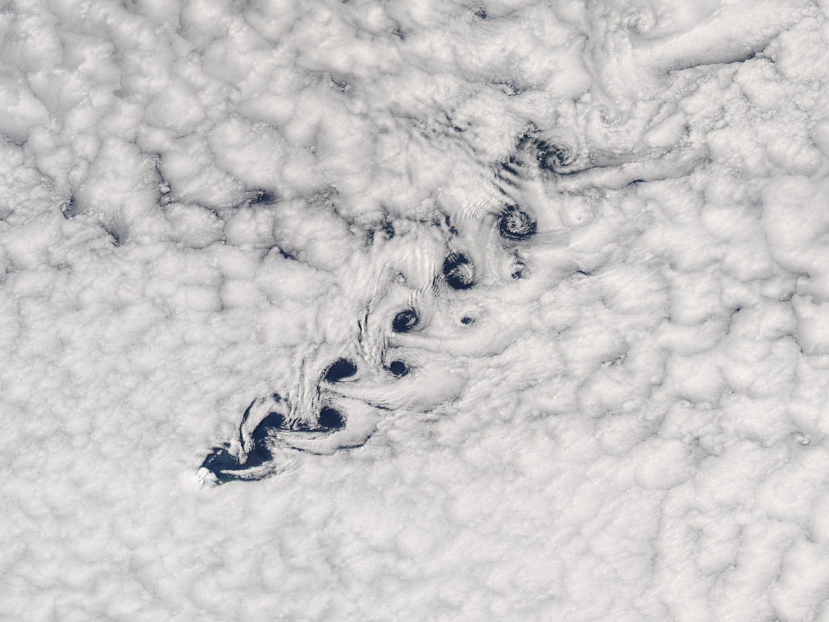 Full image from space of a blanket of white, fluffy, swirling clouds with a vortex of clouds crossing the image diagonally.