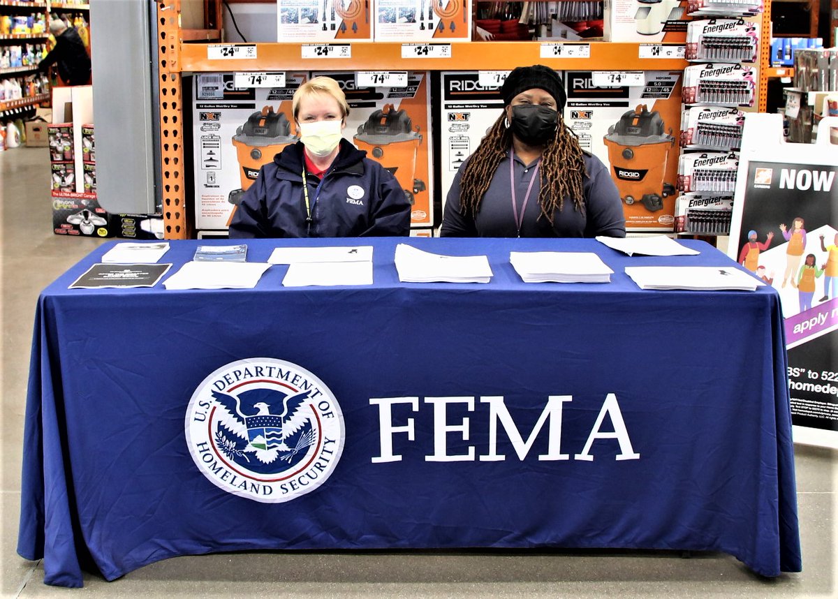 a photo of two women at a booth with publications and a FEMA blue tablecloth. 