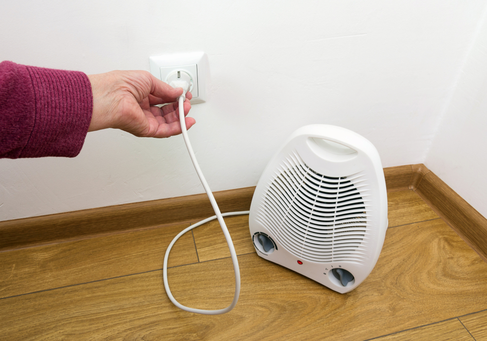 Photo of older White woman's hand plugging electric space heater into wall outlet.