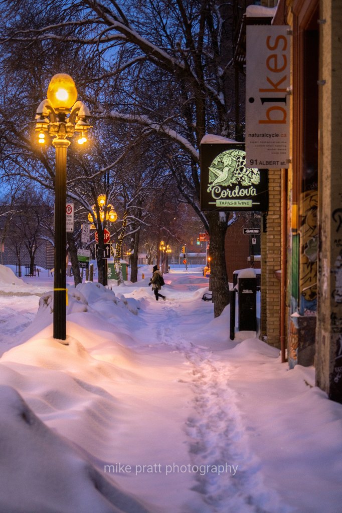 Fresh snow fallen on quiet streets in Winnipegs historic Exchange District. Vintage street lamps illuminate the area in soft amber glow.