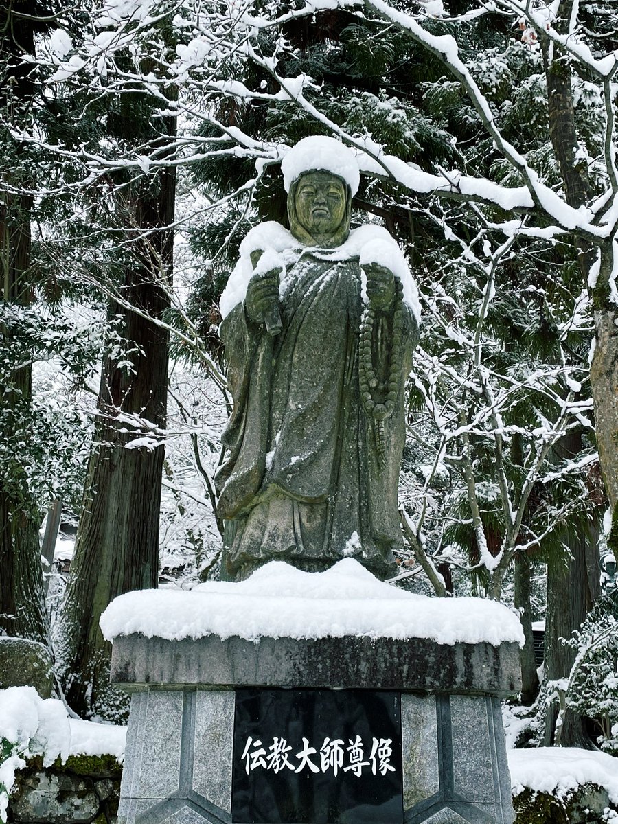 雪の伝教大師像。白くふわふわの帽子と襟巻きをお召しになっております。境内にはサラサラの粉雪が少し降っております。