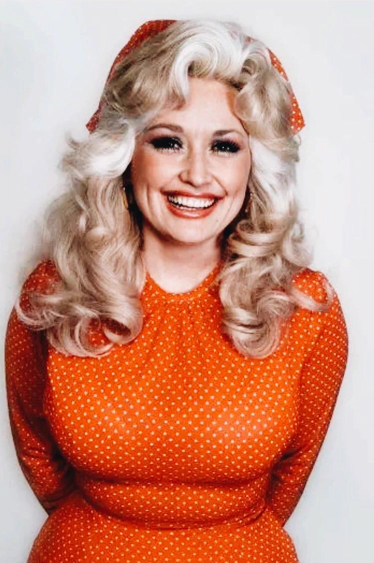 A photo of a young Dolly Parton wearing an orange and white polka dot dress.