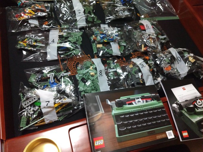 Over 10 different Lego bags numbered, some with duplicate numbers, sprawled across a game table. The thick Lego instruction booklet sits in front.
