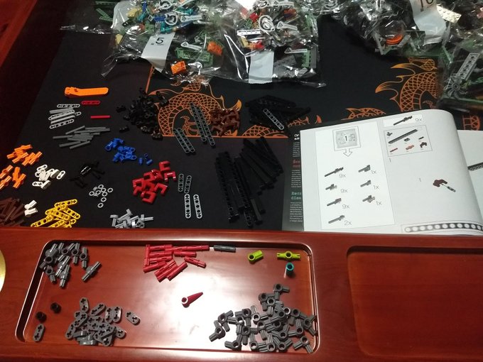 Bunches of different Lego types spread across the game table with matching items together, pile of bags in the back and instruction booklet in front