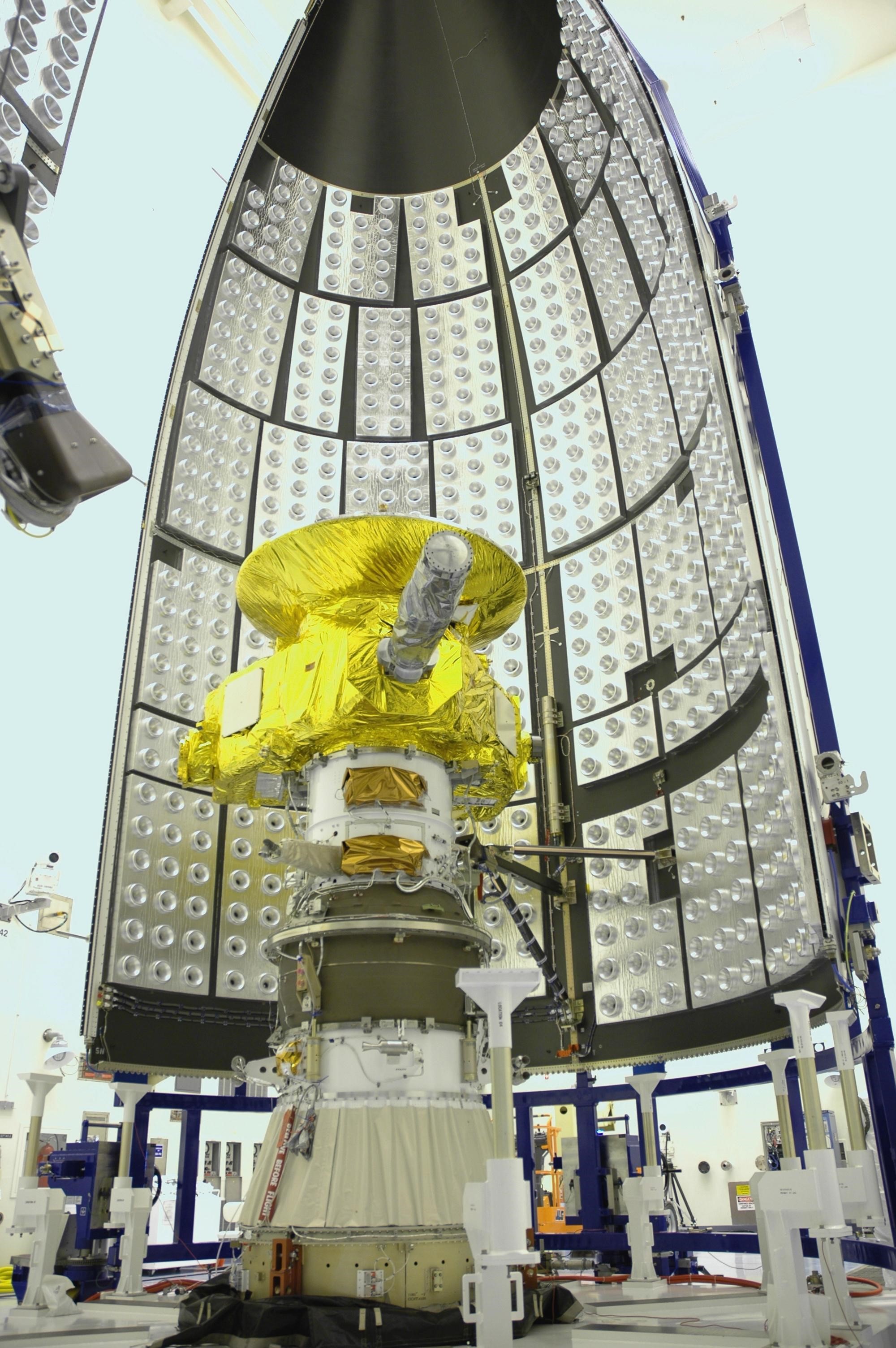 the New Horizons spacecraft, about the size of a piano and covered with gold-colored foil, about to be sealed into the rocket fairing prior launch