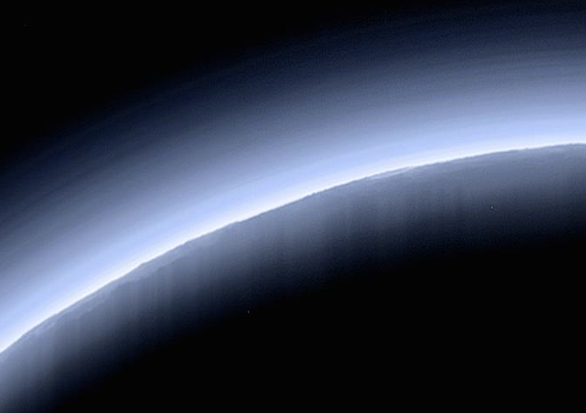 the curving horizon of Pluto, with blue layers of atmosphere visible, and mountains casting long shadows in the haze