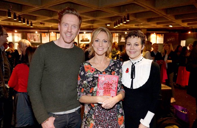 A tall, red haired, white man stands beside a white woman with blonde hair and a white woman with brunette hair. The blonde woman holds a book titled: "A Poem for Every Day".