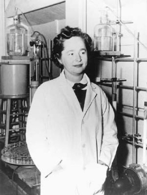 Gertrude Elion in a lab coat in front of a rack of equipment.