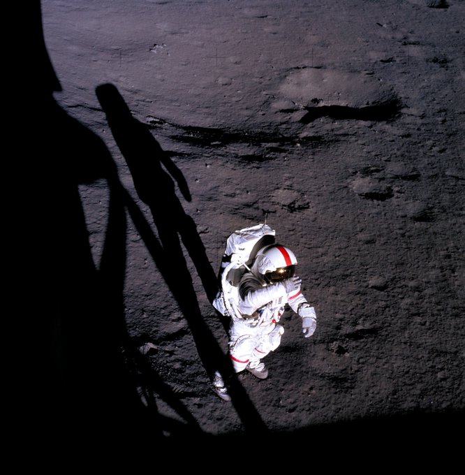 Alan Shepard in a spacesuit walks on the Moon in the shadow of the lunar module.