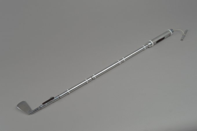 A grey makeshift golf club made from the handle of a contingency sample return device and a Wilson six-iron head. 