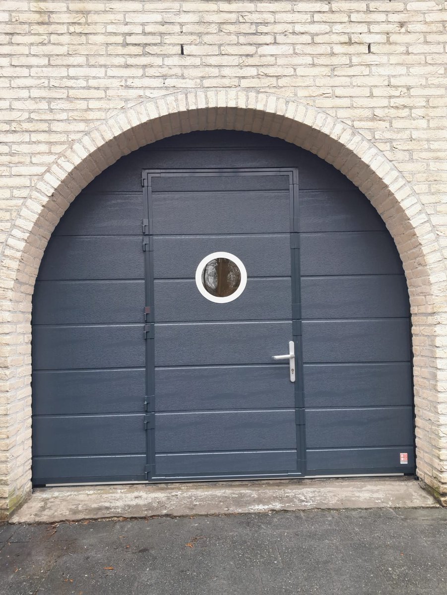 Bleyenberg_BDS's tweet photo. Een niet allerdaags plaatje.  Sectionaaldeur met ingebouwde loopdeur en voorzien van een rond rvs venster.  De toog in het metselwerk maakt nog bijzonderder. #garagedeur #isolatie #deuren https://t.co/rA3EjQeIOx