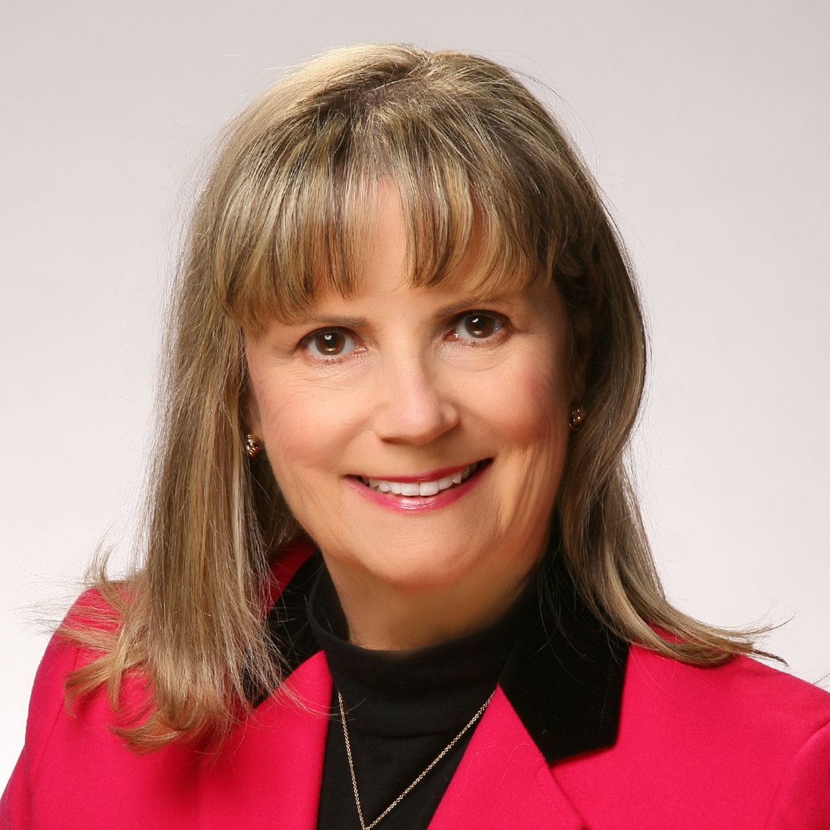 Head shot of light skinned woman with shoulder length blonde hair wearing a red jacket and a black top.