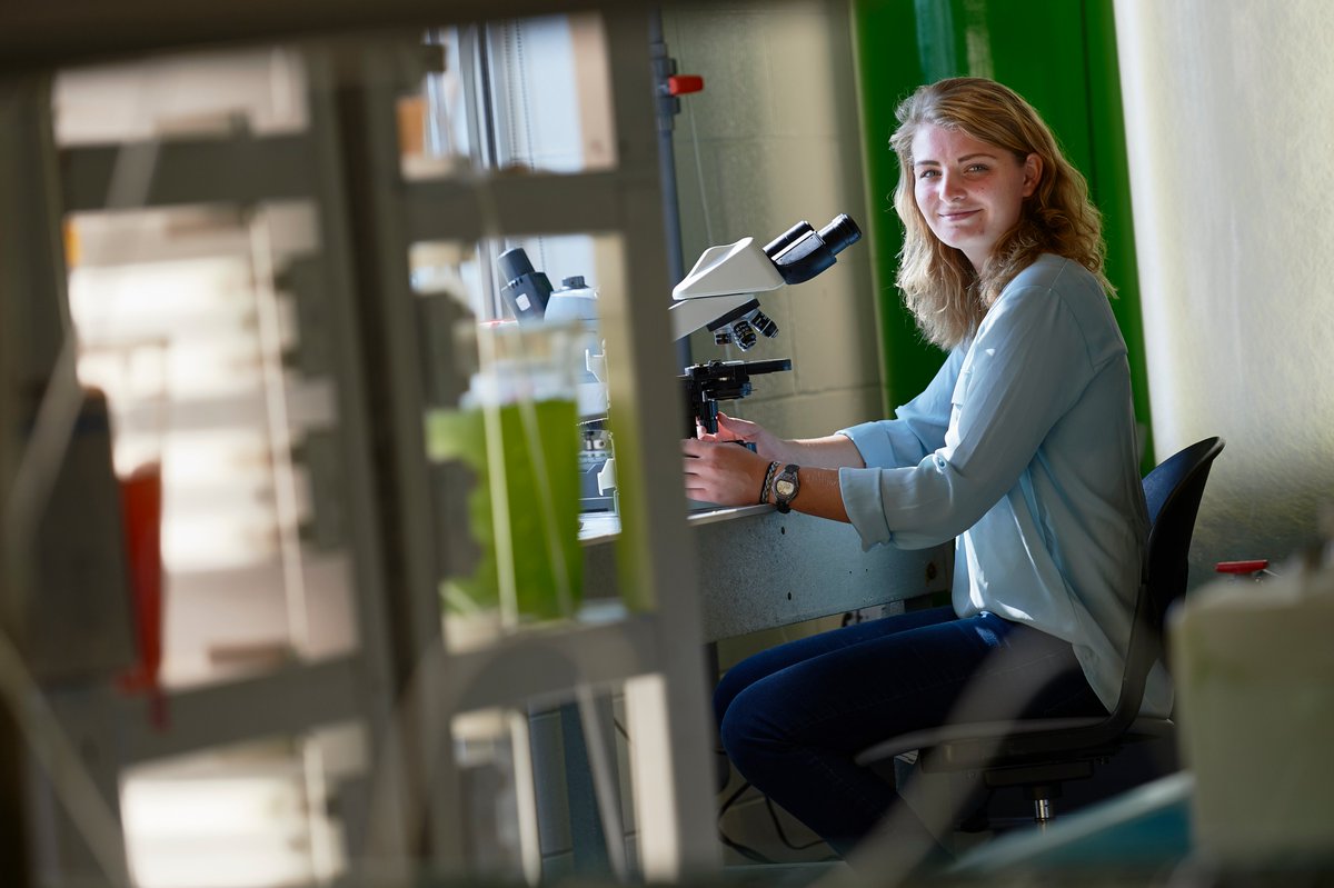 A woman sits in a lab near a microscope.