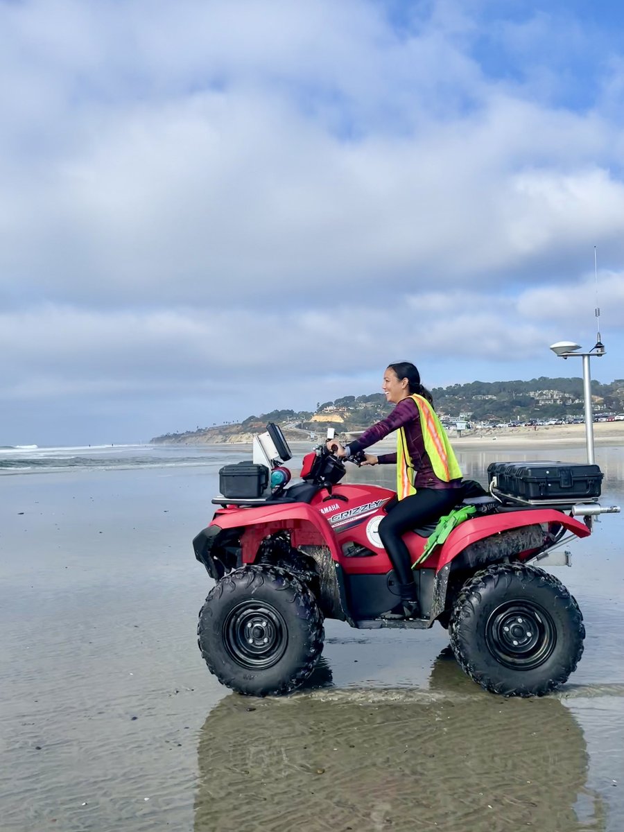 A woman scientist at the beach rides an ATV that is equipped with a GPS antenna.