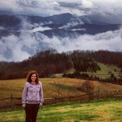 A women poses for a photo in front of a scenic mountain range.