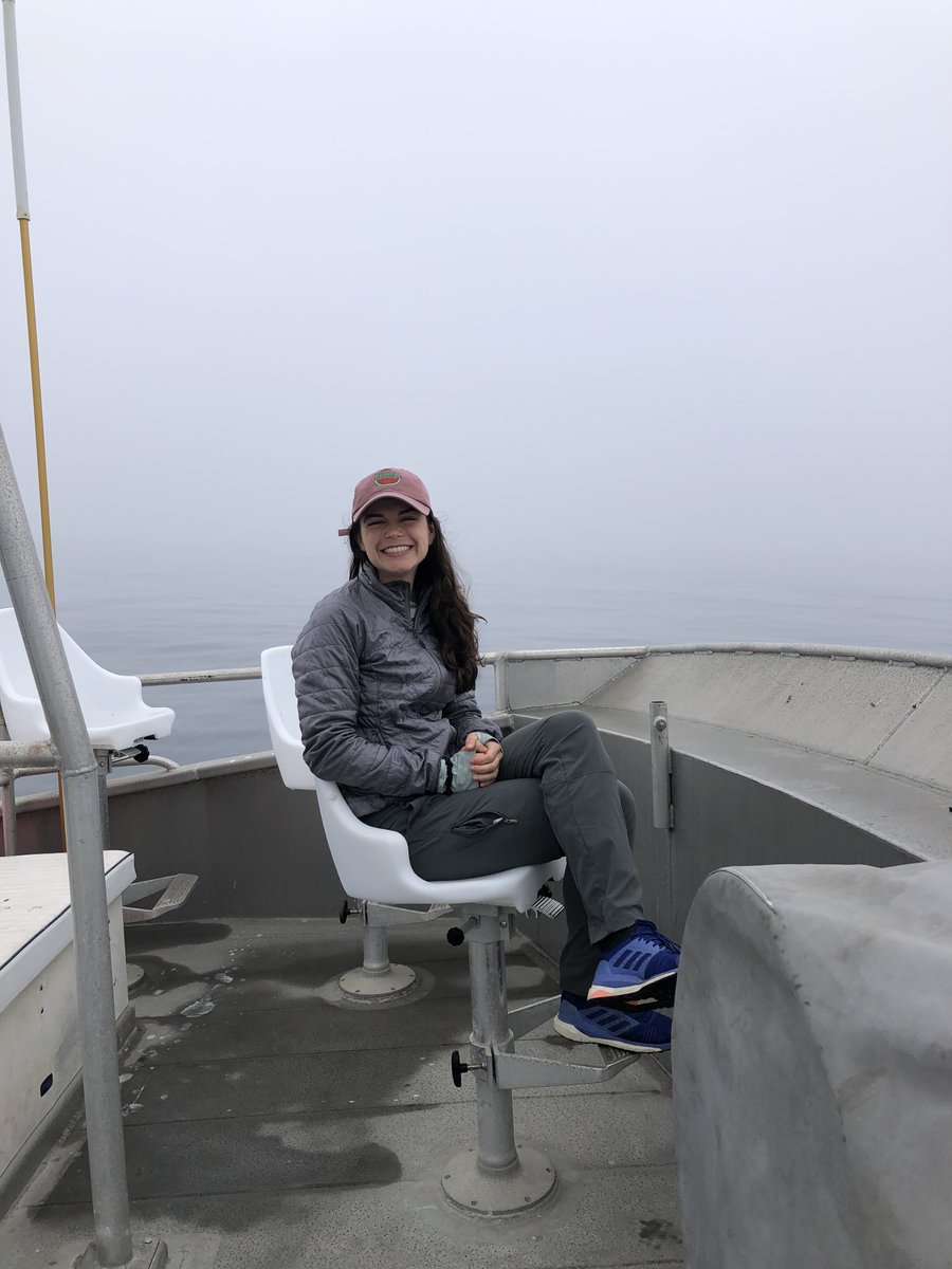 A smiling woman sits on a chair on the deck of a research vessel at sea.