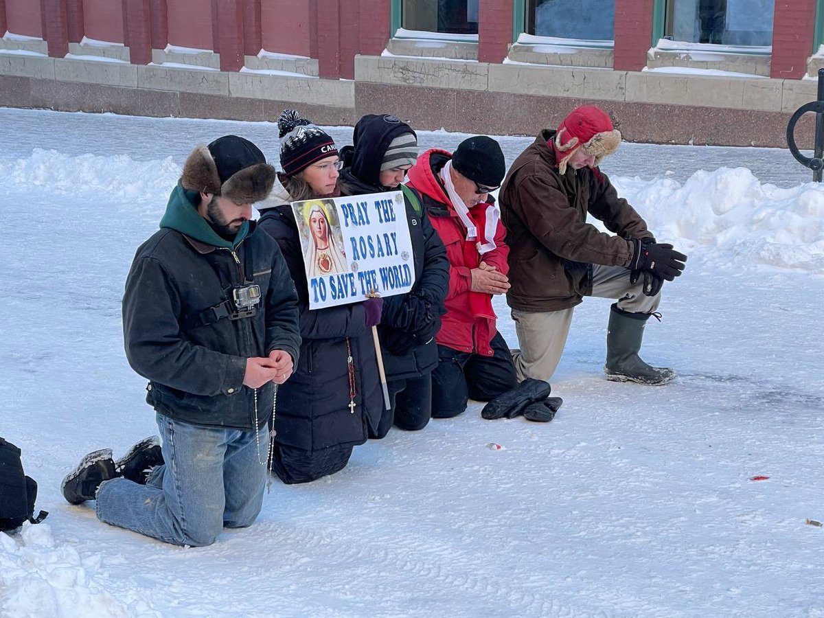 TheMarieOakes's tweet photo. A group of individuals pray in front of police in Ottawa. https://t.co/lkJ3xDn63u