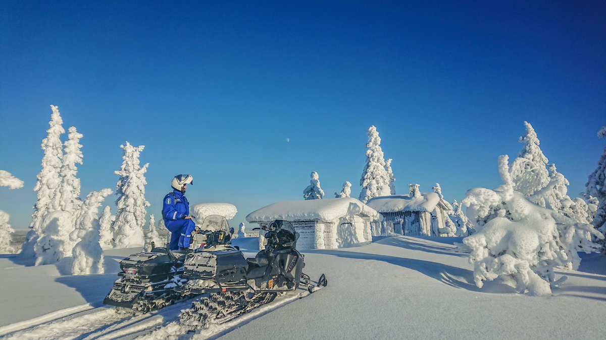 Poliisi moottorikelkan kanssa tykkylumipuiden keskellä.