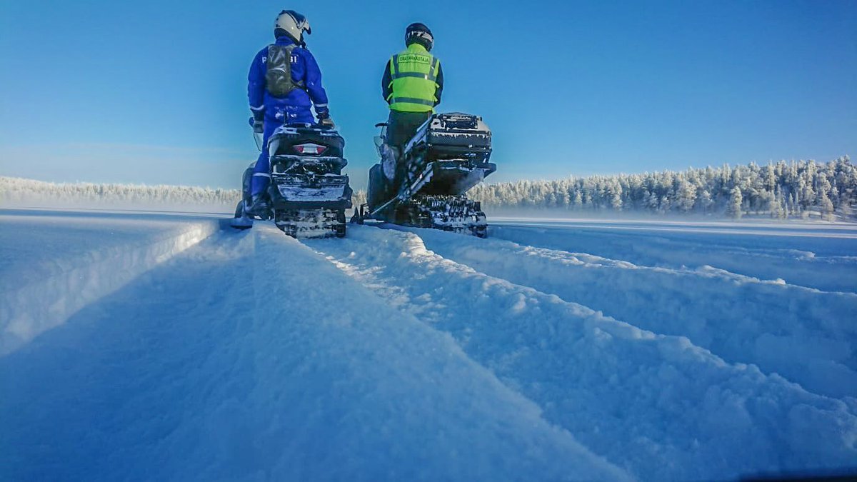 Poliisi ja erävalvoja moottorikelkoilla lumisessa maastossa.