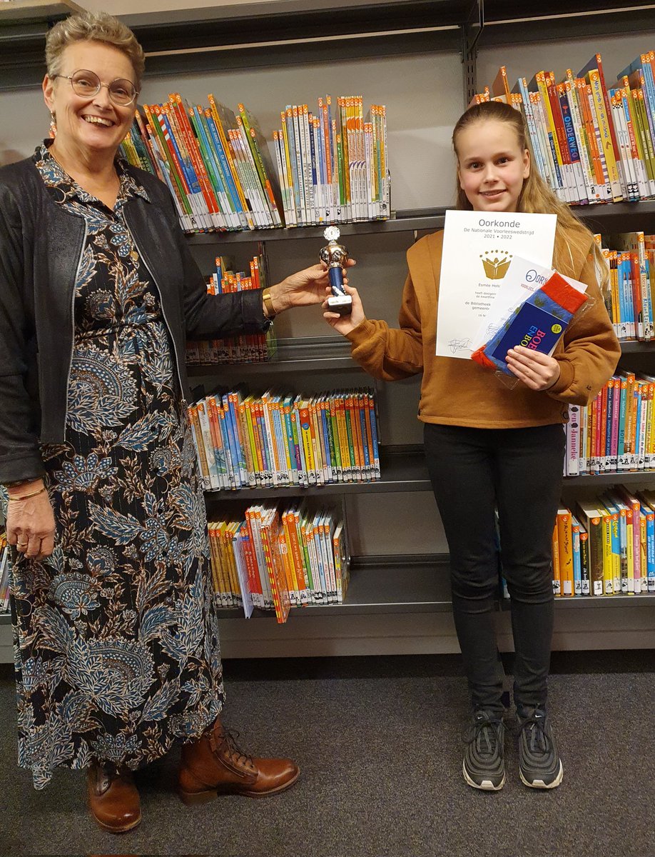 Wethouder @egvos overhandigt de beker aan Esmée Holstege. Zij wint de Voorleeswedstrijd in #Oldebroek bij @BiebNoordVeluwe. Ze koos voor een sportief fragment uit een boek geschreven door een schrijfster uit Oldebroek! Goed idee, prima voorgelezen en best bijzonder!