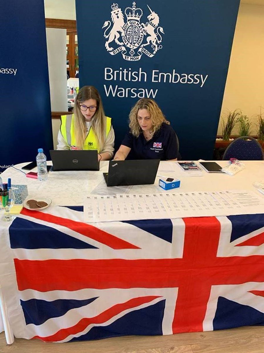 Rapid deployment team working on laptops on a table with the Union Jack, with banner in the background reading British Embassy Warsaw.