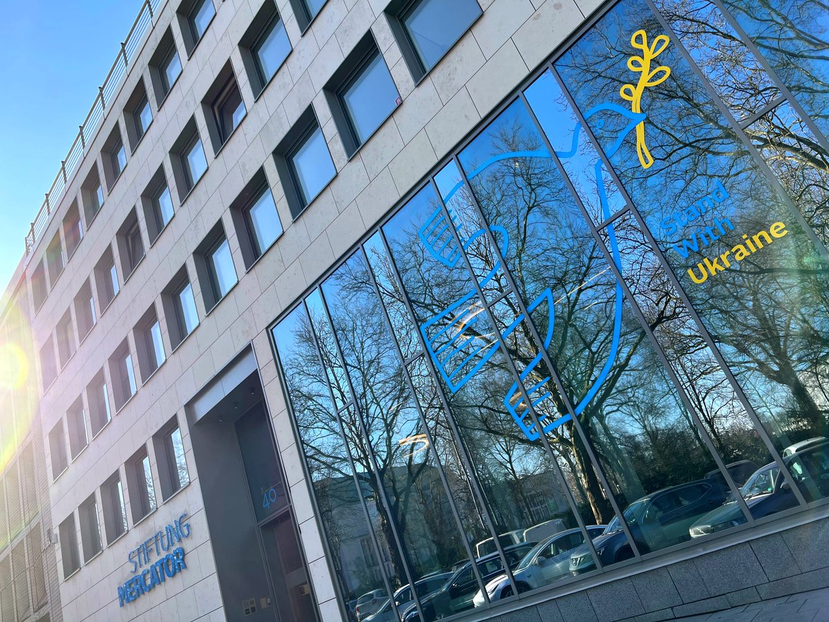 Das Gebäude der Stiftung Mercator ist zu sehen. Es hat eine große Glasfront neben dem Eingang. Auf den Fensterscheiben klebt ein Sticker: Eine blaue Taube mit gelbem Zweig im Schnabel. Das Symbol einer Friedenstaube. Darunter klebt der Sticker "Stand with Ukraine".
