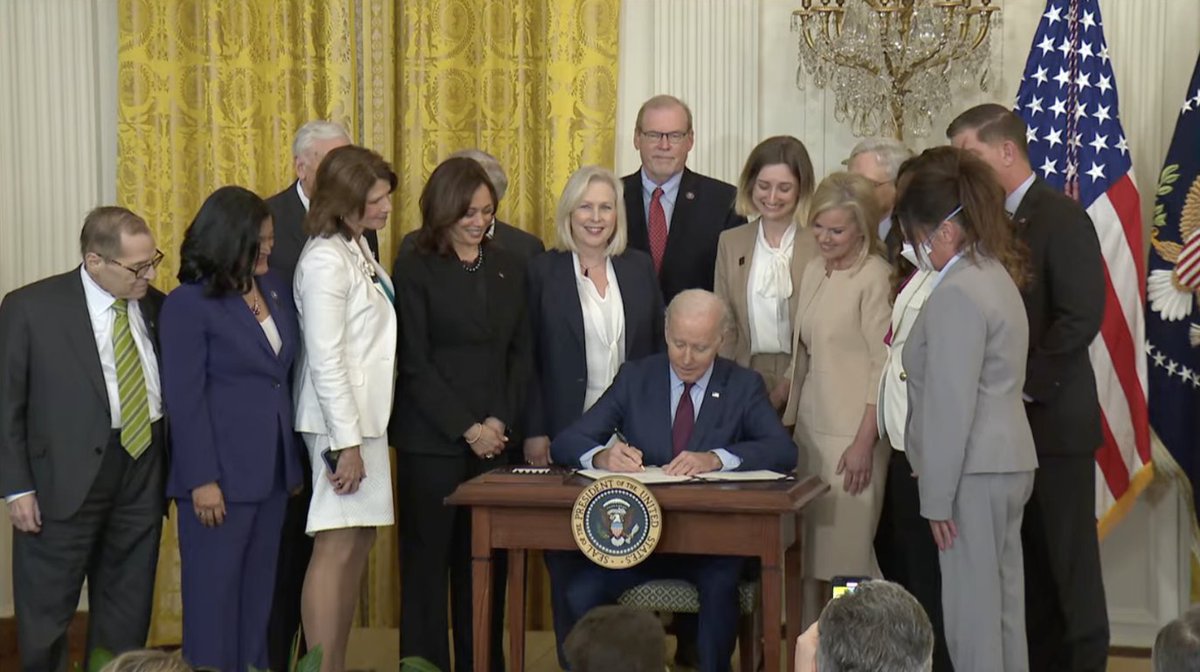 A screenshot of President Biden signing the Ending Forced Arbitration of Sexual Assault and Sexual Harassment Act, with VP Harris, lawmakers, and advocates standing behind him.