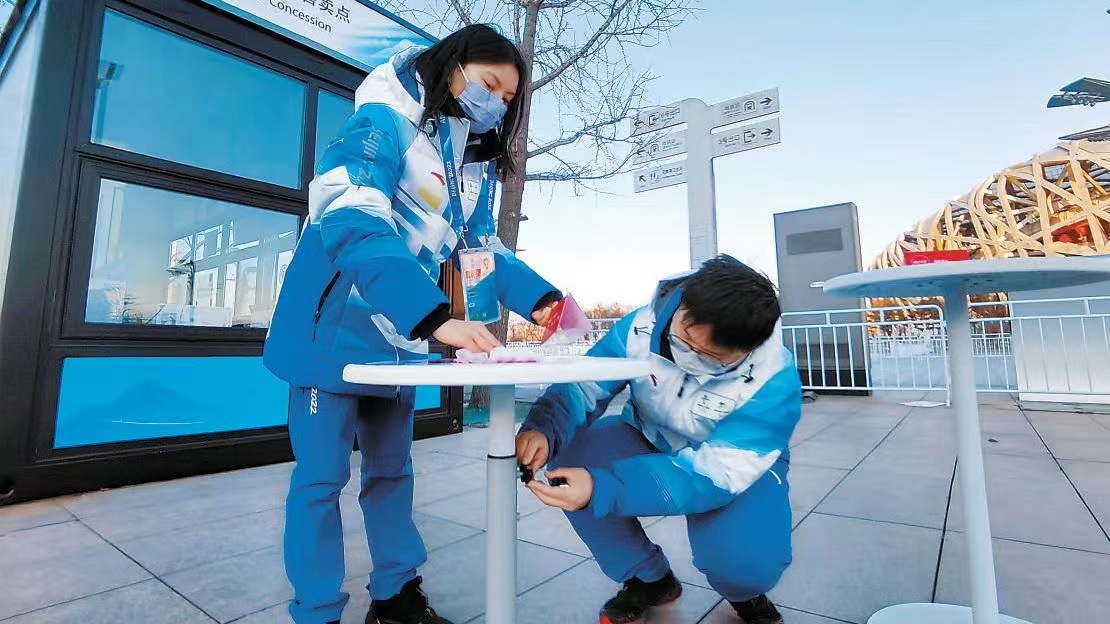 BeijingDiscover's tweet photo. In the run-up to the 2022 Beijing Paralympic Winter Games, volunteers are adjusting the height of the small round table at a barrier-free public sales point. 💕👍
#Beijing2022 #BeijingDevelopment (Photo: Beijing Daily) https://t.co/gOI9UVJ2FF